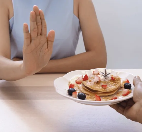 Woman pushing away a plate of pancakes with berries