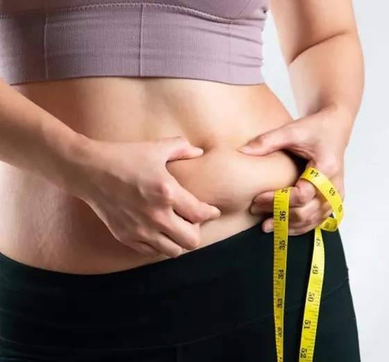 Person pinching belly fat beside a measuring tape