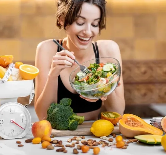 Smiling woman eating a salad at a table of fruit and vegetables